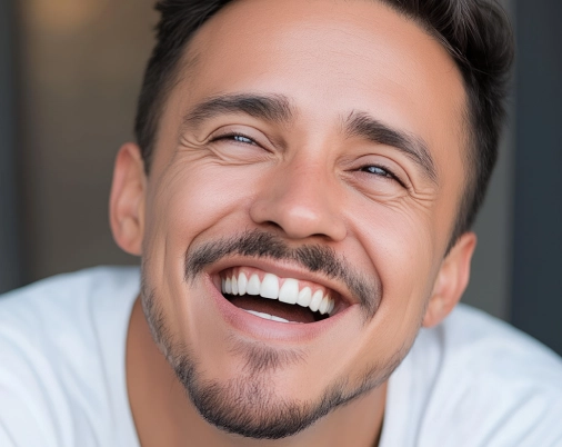 Close-up of a man with dark hair and facial hair smiling with teeth showing.